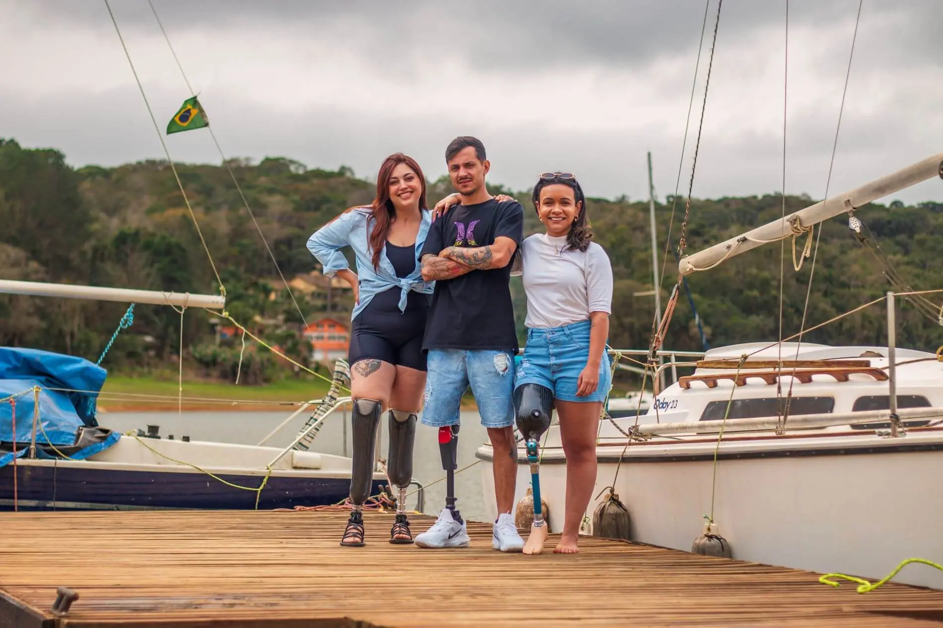 Três pacientes da Conforpés com próteses de perna, de pé no píer de uma marina