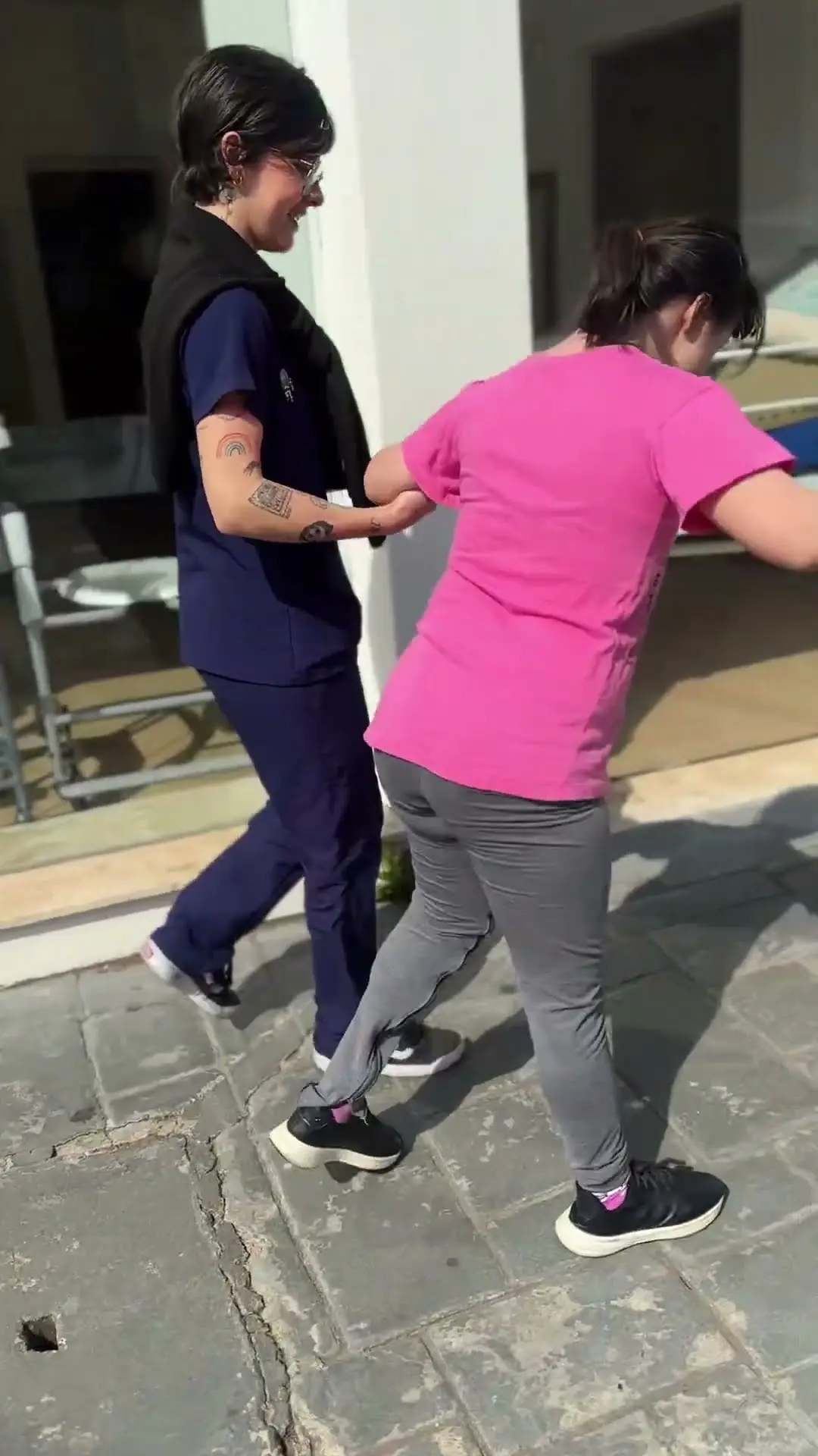 Isa caminhando na calçada com a fisioterapeuta