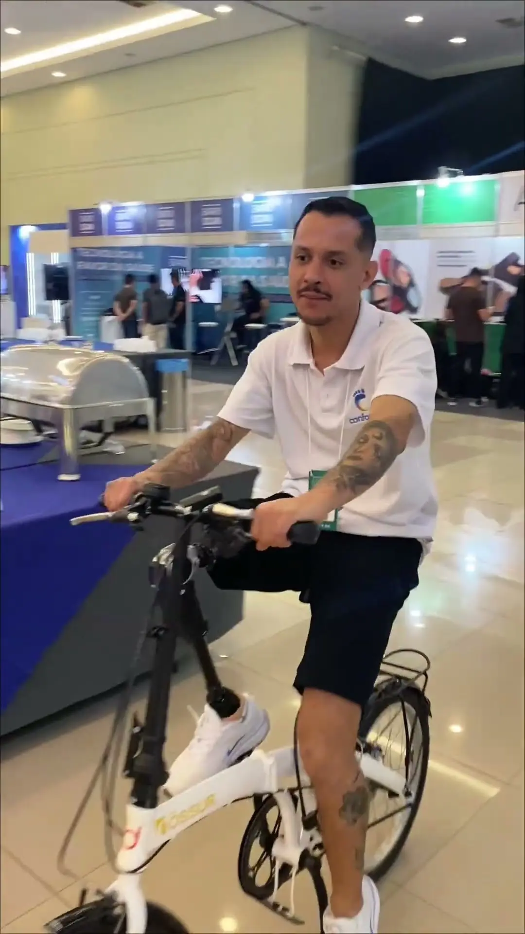 Paciente com prótese de perna pedalando uma bicicleta num estande de feira